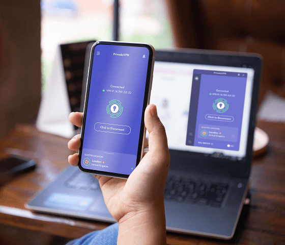 Un gros plan d’une main tenant un téléphone avec l’application PrivadoVPN dessus, devant un ordinateur portable qui affiche également l’application PrivadoVPN.