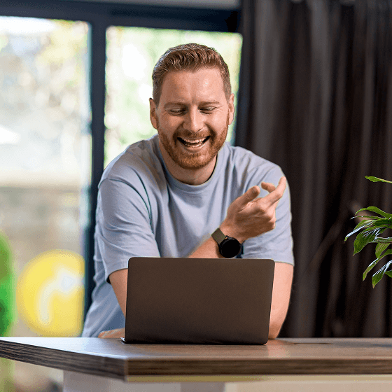Een man met een baard zit voor een laptop en lacht om iets dat hij leest in een nieuwsgroep.