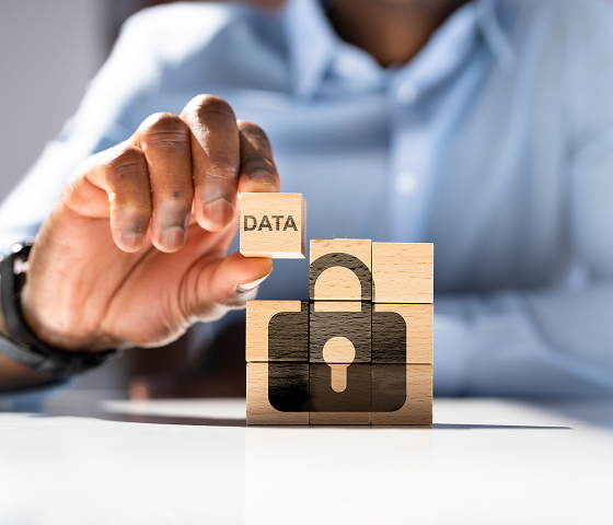 A man’s torso is visible in the frame. In his right hand, he is holding a wooden block that says, “Data” and placing it in a stack of blocks that form a black lock.