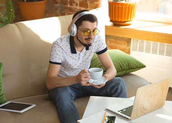 A man with a black and white polka dotted polo shirt is drinking coffee and reading his favorite newsgroups on a laptop.
