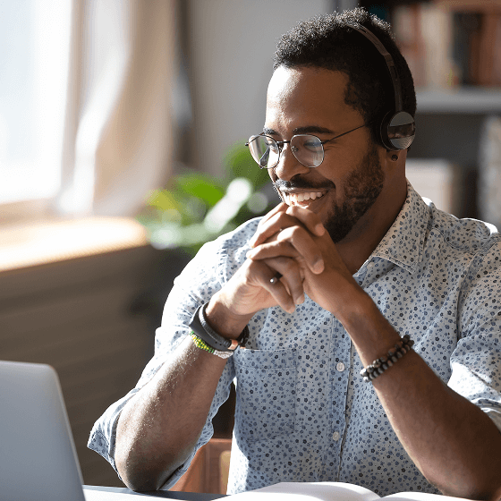 A man wearing a headset is sitting in front of a laptop, smiling as he finds the articles he wants with Tweaknews search through UsenetWire.