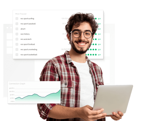 A man with round glasses and a flannel shirt is holding a laptop in both hands, smiling at the camera. He is standing in front of a window with a number of newsgroups listed on it.