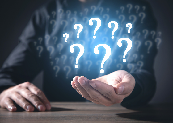 A man’s torso is visible in the frame. He is holding out his left hand, palm up, and 8 question marks are floating above it.