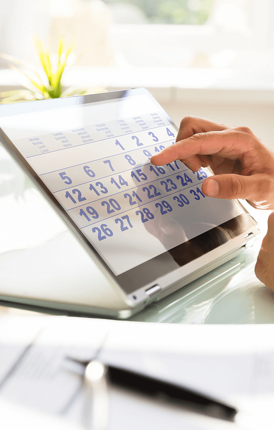 A closeup of a hand poitning to the 9th day of the month on a calendar on a laptop screen.