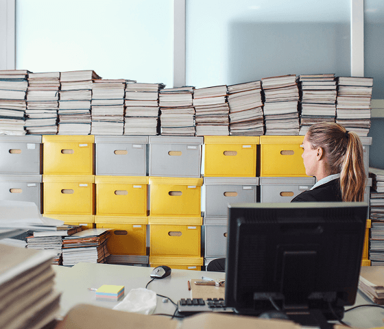 A woman in an office is looking at a wall of bank boxes and files stacked behind her.