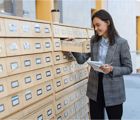 A woman wearing an really nice twead jacket is flipping through a card catalogue.